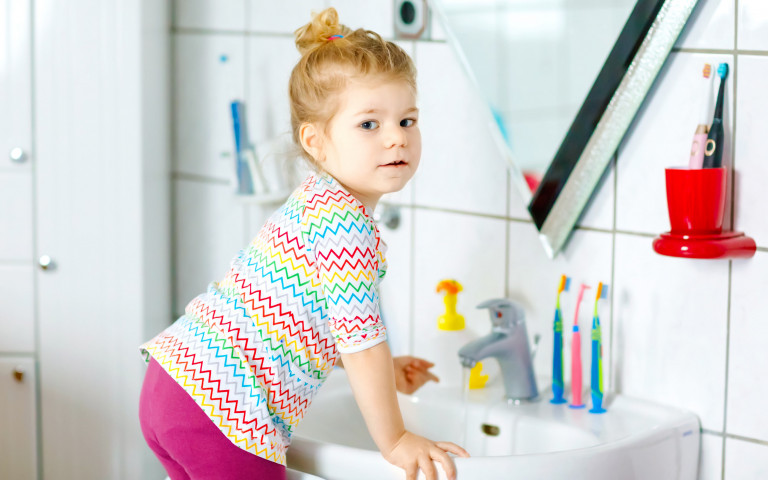 klein meisje aan spiegel in badkamer met tandenborstels