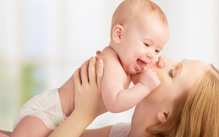 bébé dans les bras de maman et maman qui lui fait un bisous