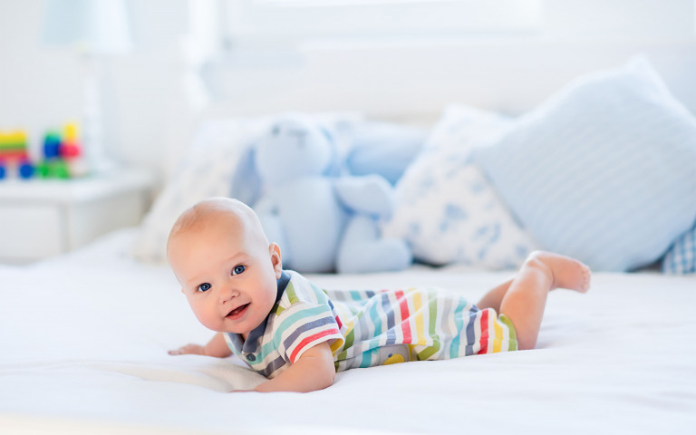 Baby ligt op zijn buik op een bed