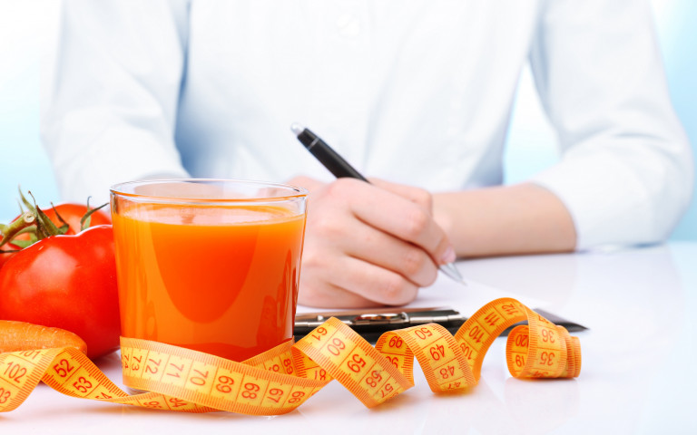 Diététicienne qui élabore un plan diététique avec un jus de tomates et un mètre ruban