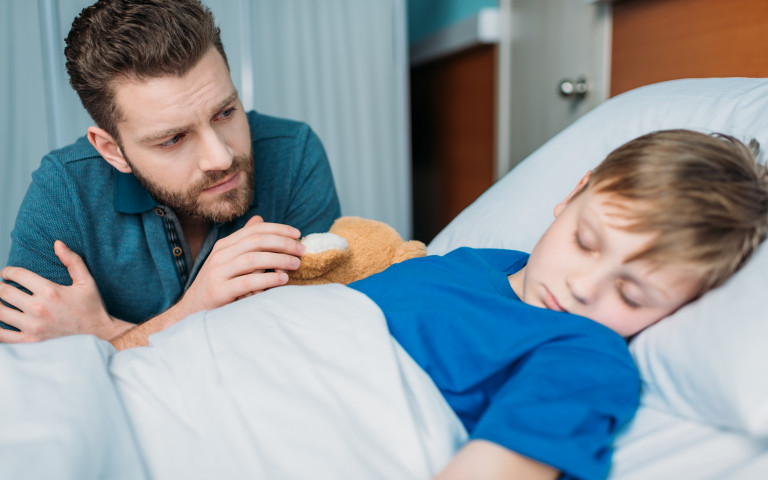 Enfant malade hospitalisé qui dort avec son papa à son chevet