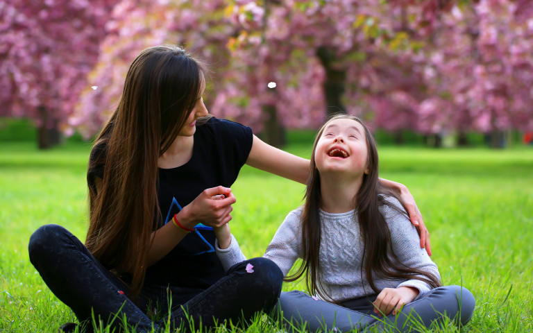 Lachend meisje met down met mama in park met bloesems