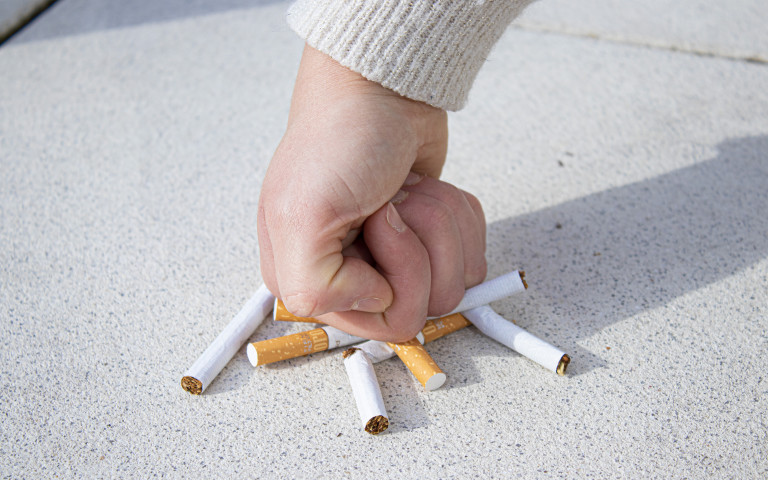 Vuist breekt een hoopje sigaretten op de grond