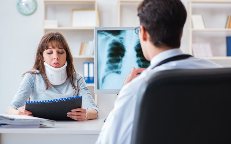 Vrouw met brace om nek bij dokter met x-ray
