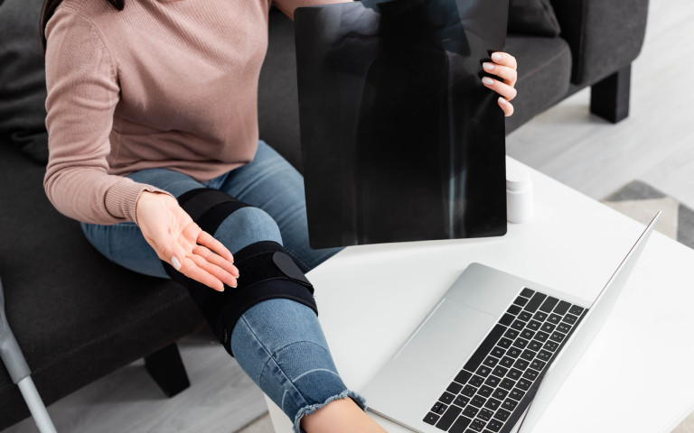 vrouw met brace aan knie werkt op laptop