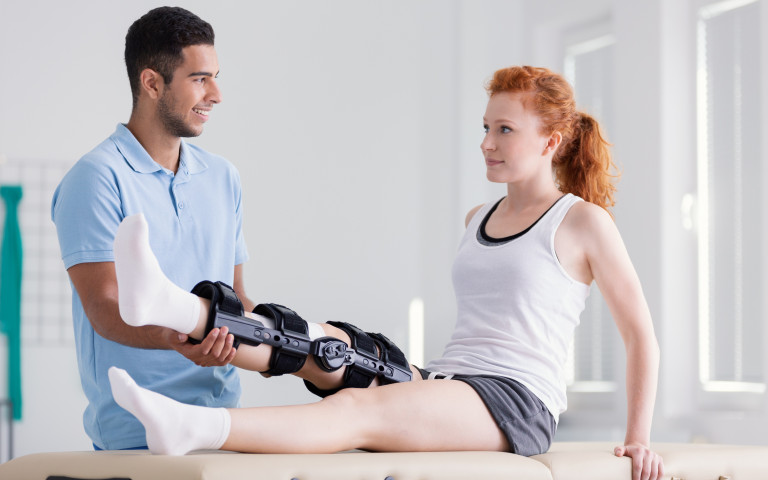 jonge vrouw met brace aan knie bij dokter of kine