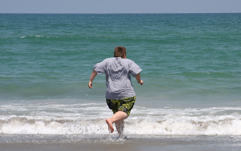 Jongen met overgewicht loopt de zee in