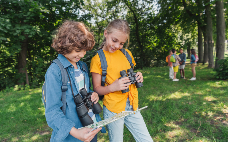 Kinderen met verrekijker in bos bekijken landkaart
