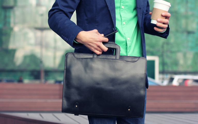 Man met aktentas, smartphone en koffie voor gebouw