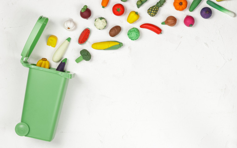Divers légumes jetés en direction d'une poubelle verte