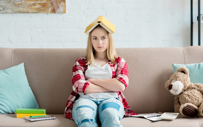 Studente zit in zetel met gekruiste armen en boek op haar hoofd