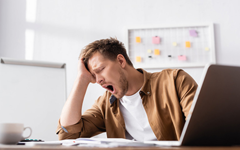 Homme bâillant derrière l'écran de son ordinateur portable