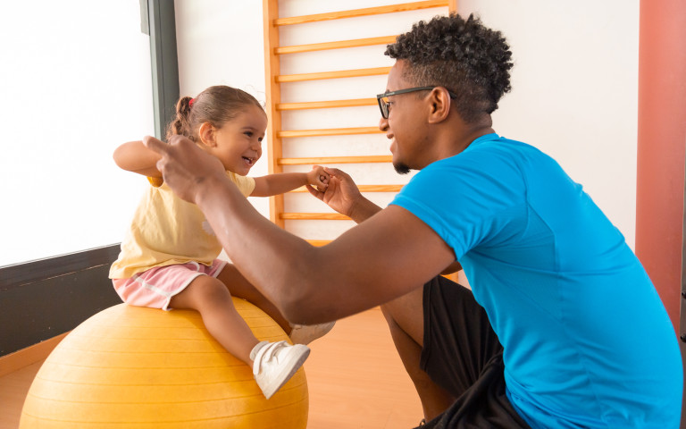 Papa en dochter bewegen samen, dochter zit op een zitbal