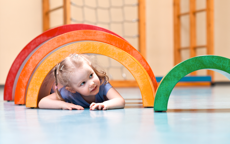 Kleuter kruipt onder gekleurde bogen in de turnzaal