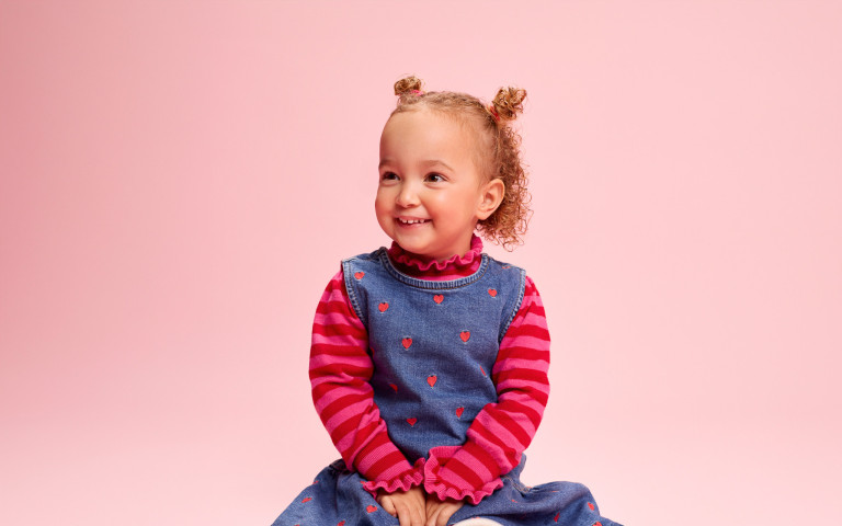 Kleuter met krulletjes lacht op roze achtergrond