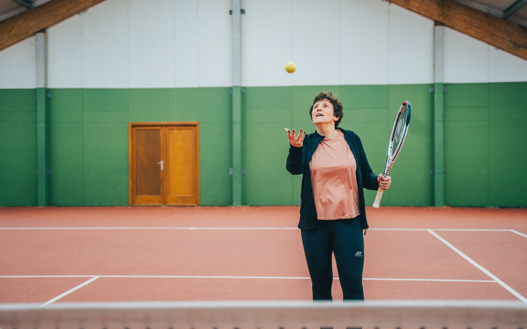 Katy gooit bal omhoog en heeft tennisraket vast op tennisplein
