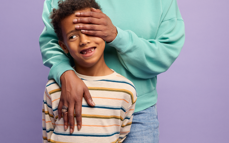 Kind lacht ondeugend, mama bedekt deel van zijn gezicht