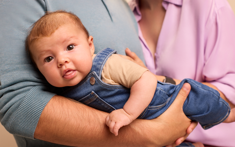 Baby kijkt naar de camera, ligt op de arm van de papa
