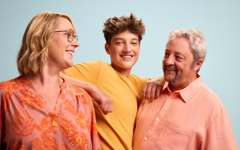 LevensMomenten fotoshoot, gezin met zoon, mama en grootvader, allemaal met zomers kleurige kledij aan op een lichtblauwe achtergrond