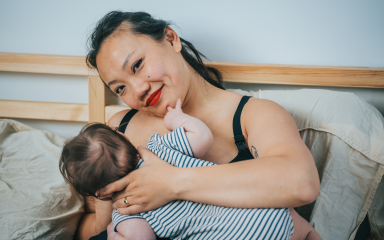 Baby Remus drinkt aan de borst van mama Tseu, Tseu lacht en kijkt naar de camera