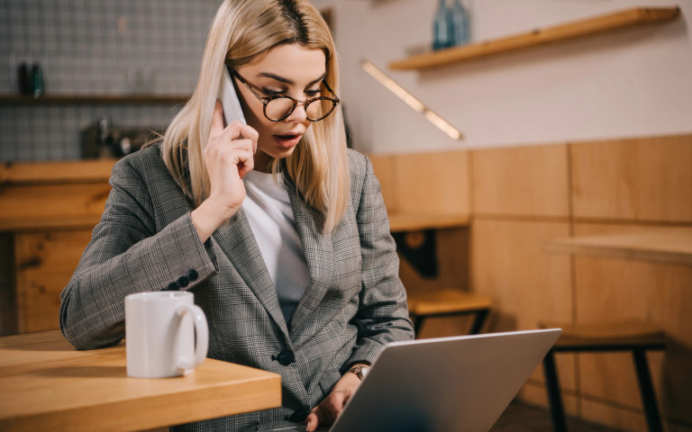 Vrouw bekijkt laptop terwijl ze telefoneert.