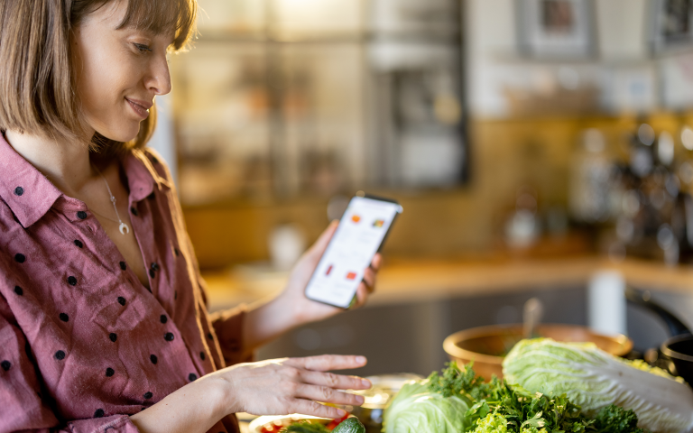 vrouw checkt app en bekijkt haar groenten op tafel
