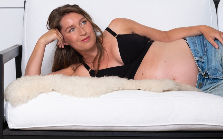 Zwangere vrouw ligt dwars neer op de zetel met een zwarte Feelou zwangerschapsbh aan