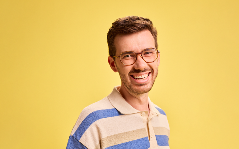 Man rond de 25 jaar lacht naar de camera, gele achtergrond