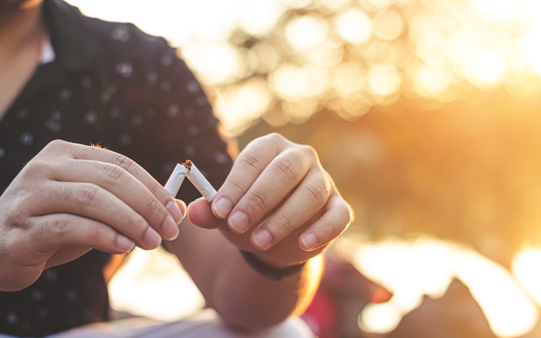 Man wil stoppen met roken en zit buiten in de zomerzon, breekt een sigeret in twee