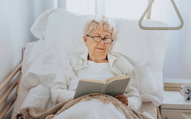 Senior vrouw zit rechtop in een verzorgingsbed te lezen