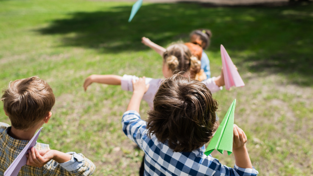 Kinderen spelen buiten en gooien met papieren vliegtuigjes