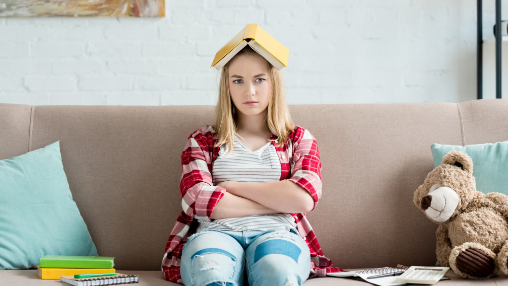 Studente zit in zetel met gekruiste armen en boek op haar hoofd