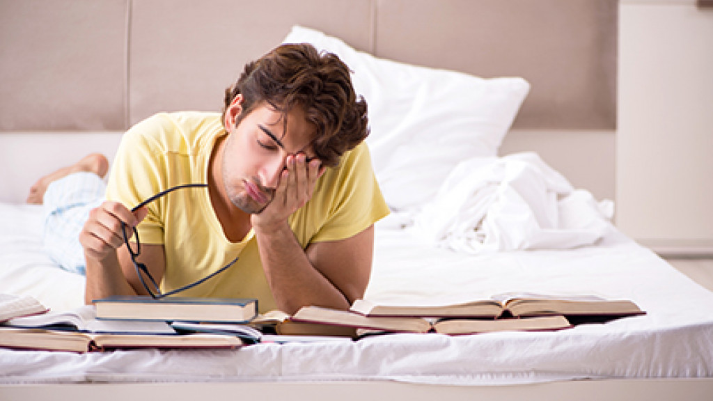 Jeune étudiant qui étudie sur son lit