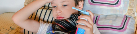 enfant malade dans son lit qui tient un spray médicament dans sa main