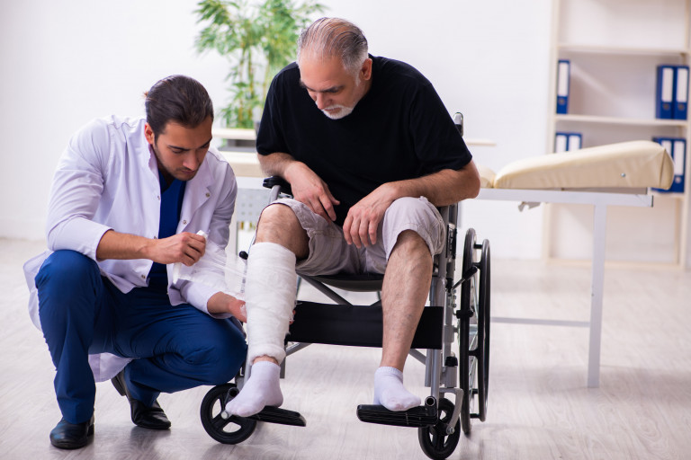 man met gebroken been in rolstoel