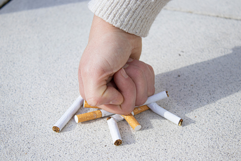 Vuist breekt een hoopje sigaretten op de grond