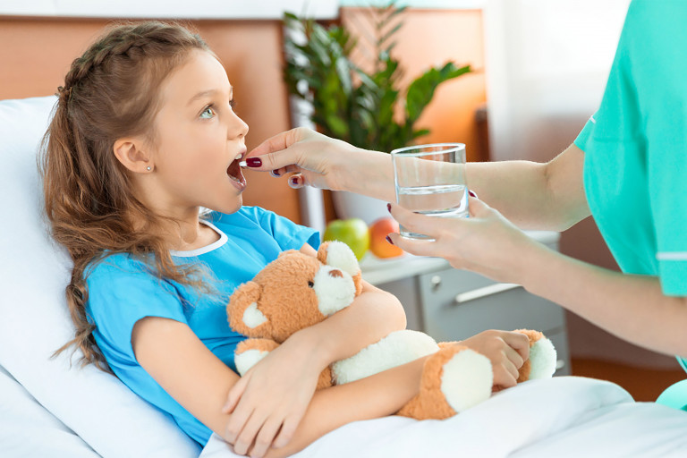 Ziek meisje met knuffel in de hand krijgt medicatie in het ziekenhuis door een verpleegster