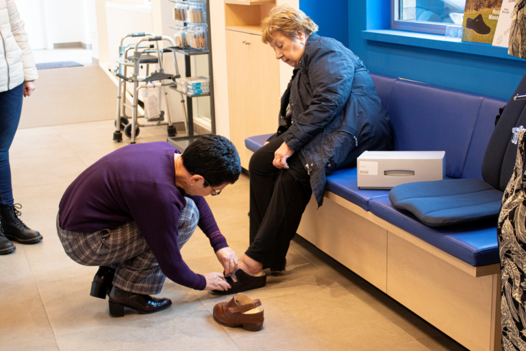 Medewerker van de winkel van Zorgboetiek in Aalst helpt een klant die schoenen past.