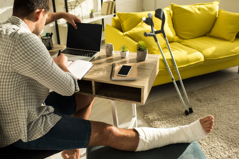 man met been in gips werkt op laptop