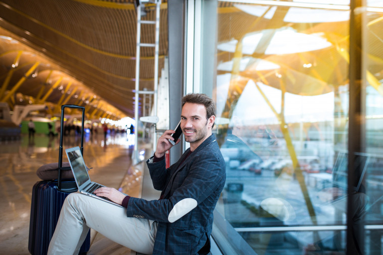 man met smartphone werkt op laptop in luchthaven
