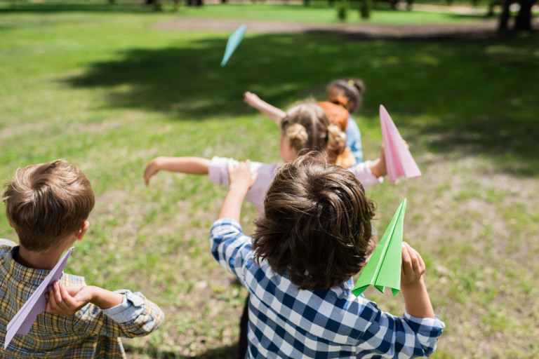 Kinderen spelen buiten en gooien met papieren vliegtuigjes