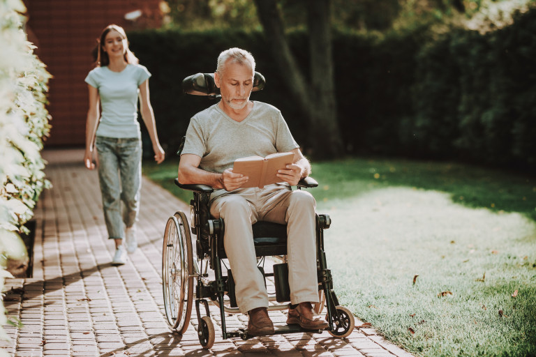 Man leest boek in rolstoel buiten