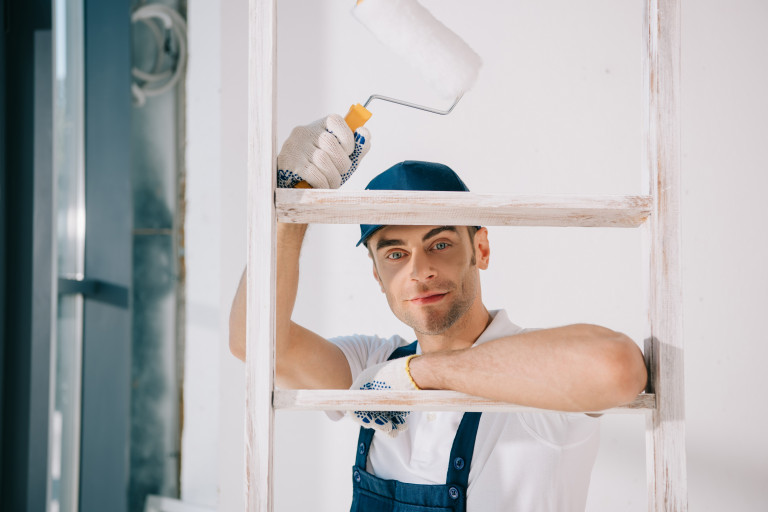 Schilder op ladder met verfrol in de hand