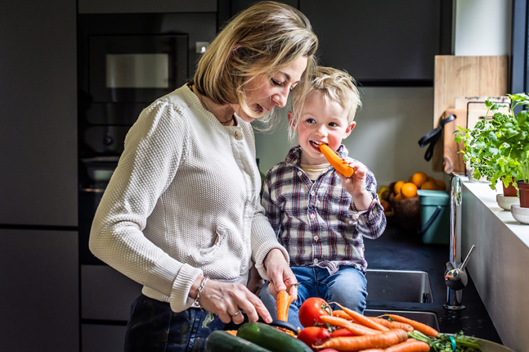 Mama en kleuter aan de wastafel groenten aan het snijden