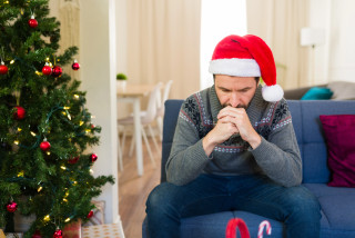 Mentale gezondheid man zit met kerstmuts aan kerstboom